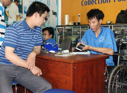 Anh Trần Văn Thái (phải, 33 tuổi, ở TP.Vũng Tàu), dù đôi chân tật nguyền vẫn làm người quản lý tại cửa hàng sửa chữa điện thoại di động của Công ty Truyền Tín.