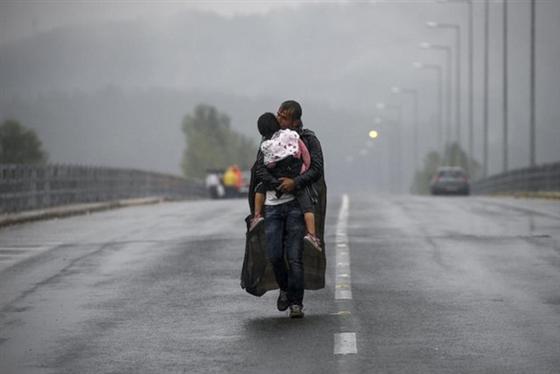 Một người đàn ông Syria ôm con gái và đi về phía biên giới Hy Lạp – Macedonia dưới cơn mưa lớn ngày 10/9/2015.