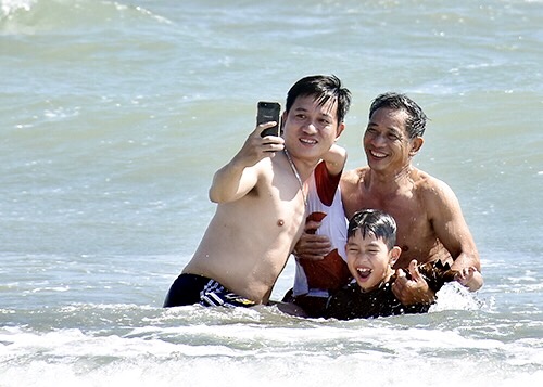 Một gia đình 3 thế hệ vừa tắm biển và vừa chụp hình.