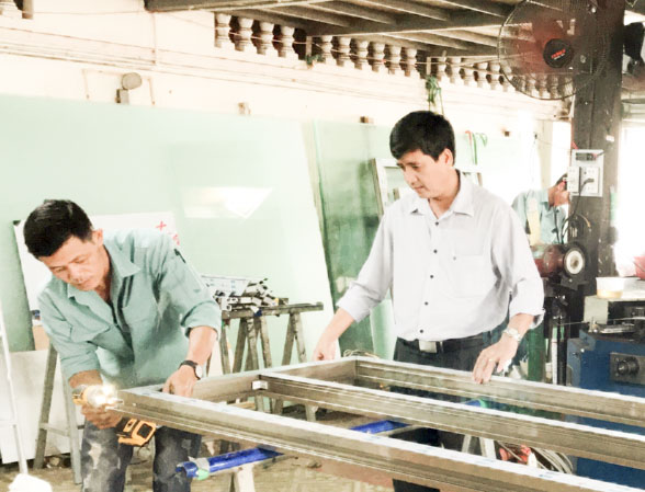 Ông Vũ Viết Nhâm (phải), Giám đốc Công ty TNHH TM-SX Thịnh Long hướng dẫn công nhân lắp ráp cửa nhôm kính.