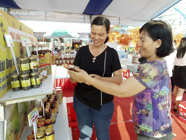 Đại diện cơ sở sản xuất mật ong Anh Tiến (bìa phải) giới thiệu sản phẩm với khách hàng tại Hội chợ kết nối giao thương.