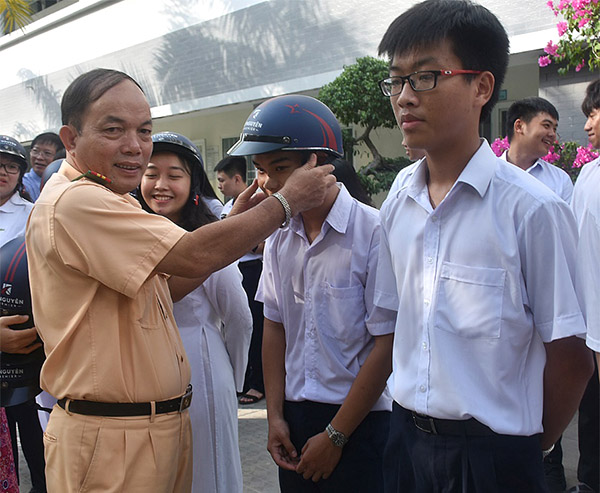 Trung tá Mai Văn Lèo, Phó đội Tuyên truyền và Xử lý TNGT thuộc Phòng PC08 trao mũ bảo hiểm cho học sinh. 