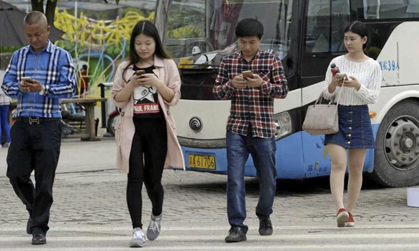 Người đi bộ xem điện thoại khi sang đường ở Trùng Khánh, Trung Quốc. 