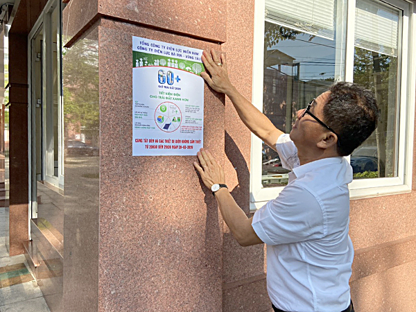 Nhân viên Công ty Điện lực BR-VT dán poster tuyên truyền về Chiến dịch Giờ Trái đất 2020 trước cổng trụ sở.
