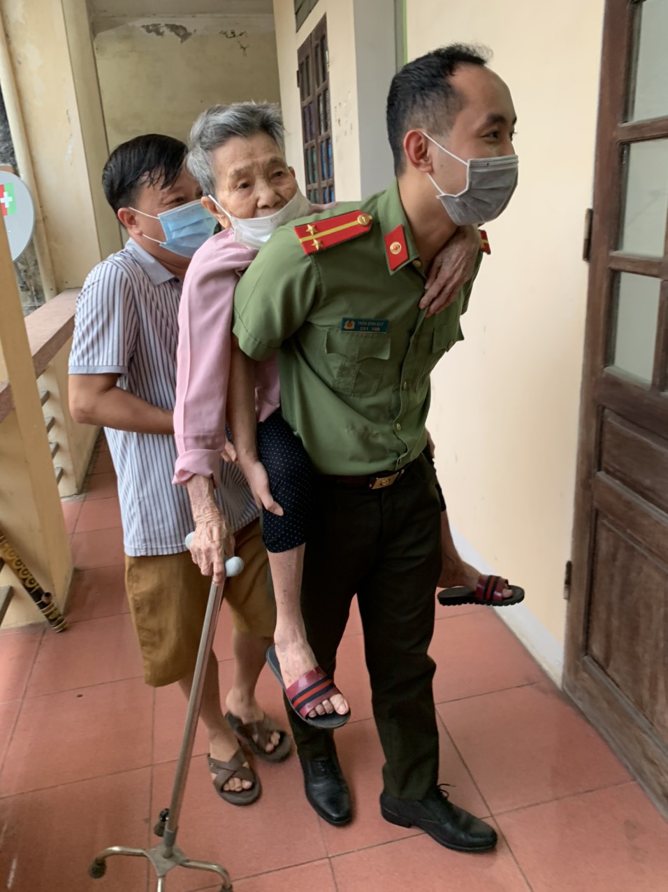 Cán bộ Công an thành phố Vinh cõng người già yếu vào  điểm làm căn cước công dân ở trung tâm xã