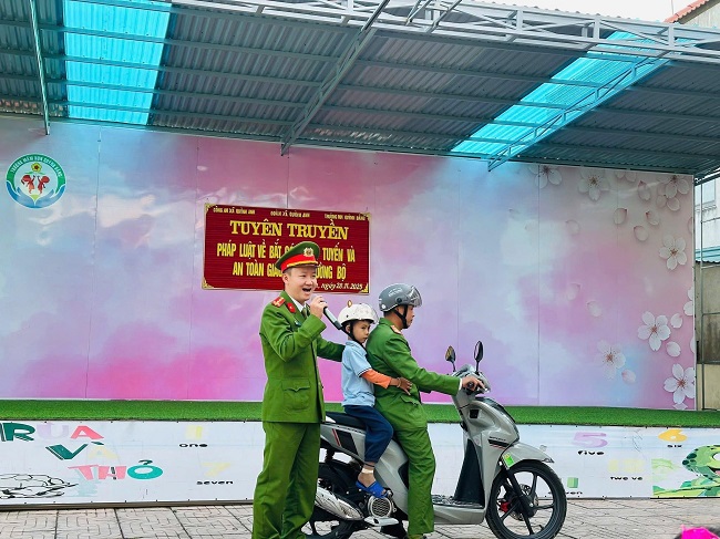 Cán bộ Công an xã Quỳnh Anh hướng dẫn học sinh đội mũ bảo hiểm đúng cách