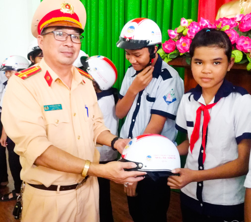 Trung tá Nguyễn Duy Bình, Đội trưởng Đội tuyên truyền và xử lý TNGT Phòng PC08 tặng mũ bảo hiểm cho học sinh.