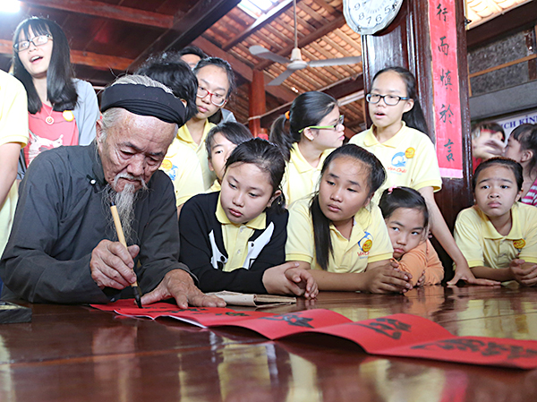 Các em nhỏ tham gia chương trình Tết yêu thương chăm chú xem ông đồ viết liễn tại Nhà Lớn Long Sơn. Ảnh: MINH THANH