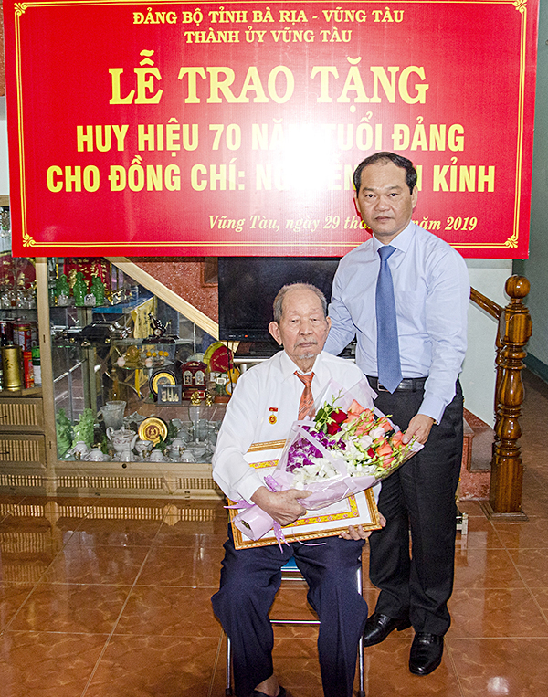 Đồng chí Mai Ngọc Thuận trao Huy hiệu 70 năm tuổi Đảng và tặng hoa chúc mừng đảng viên Nguyễn Văn Kỉnh.