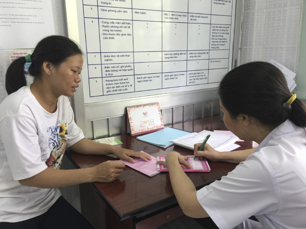 Cán bộ y tế ghi thông tin, điền kết quả thăm khám cho bà bầu vào sổ tại Trung tâm Chăm sóc Sức khỏe sinh sản tỉnh. 
