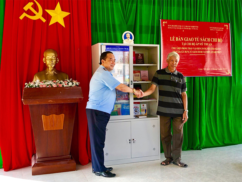 Ông Trần Văn Danh, Bí thư Đảng ủy, Cục trưởng Cục Hải quan tỉnh (bên trái) bàn giao tủ sách cho Chi bộ ấp Mỹ Thuận thuộc Đảng ủy xã Long Mỹ (huyện Đất Đỏ).