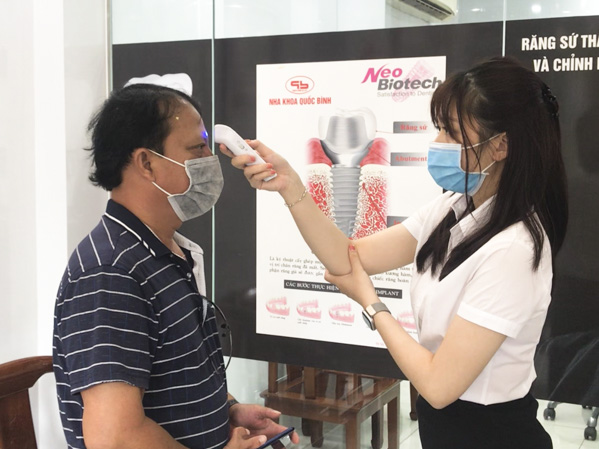 Chị Trần Thị Bảo Trân, nhân viên lễ tân Nha khoa Quốc Bình (TP. Vũng Tàu), đeo khẩu trang và đo thân nhiệt khách hàng khi đến phòng khám. Ảnh: MINH THANH