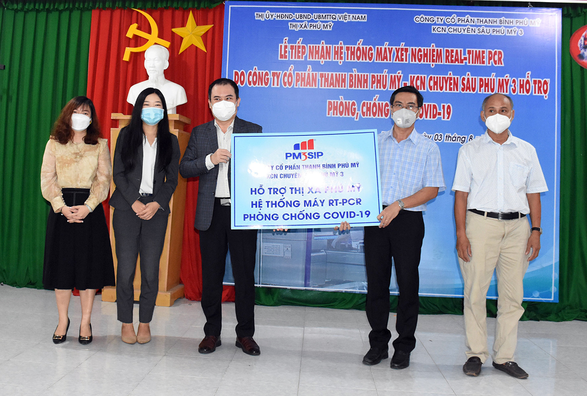Ông Tạ Quốc Bảo, Phó Tổng Giám đốc Công ty CP Thanh Bình - Phú Mỹ (thứ ba từ trái qua) trao bảng tượng trưng hỗ trợ hệ thống máy xét nghiệm RT-PCR cho ông Nguyễn Thành Nam, Phó Chủ tịch UBND TX. Phú Mỹ