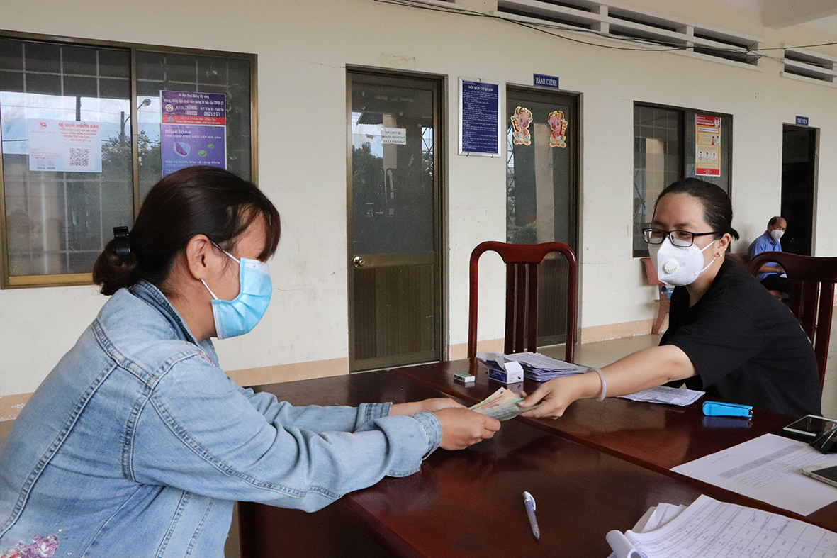 Bà Lý Thanh Huyền, cán bộ phụ trách công tác giảm nghèo UBND xã An Ngãi (bên phải) chi số tiền 1,5 triệu đồng cho bà Phạm Thị Huyền Nga (ấp An Lộc, xã An Ngãi) – lao động bị ảnh hưởng bởi dịch COVID-19.