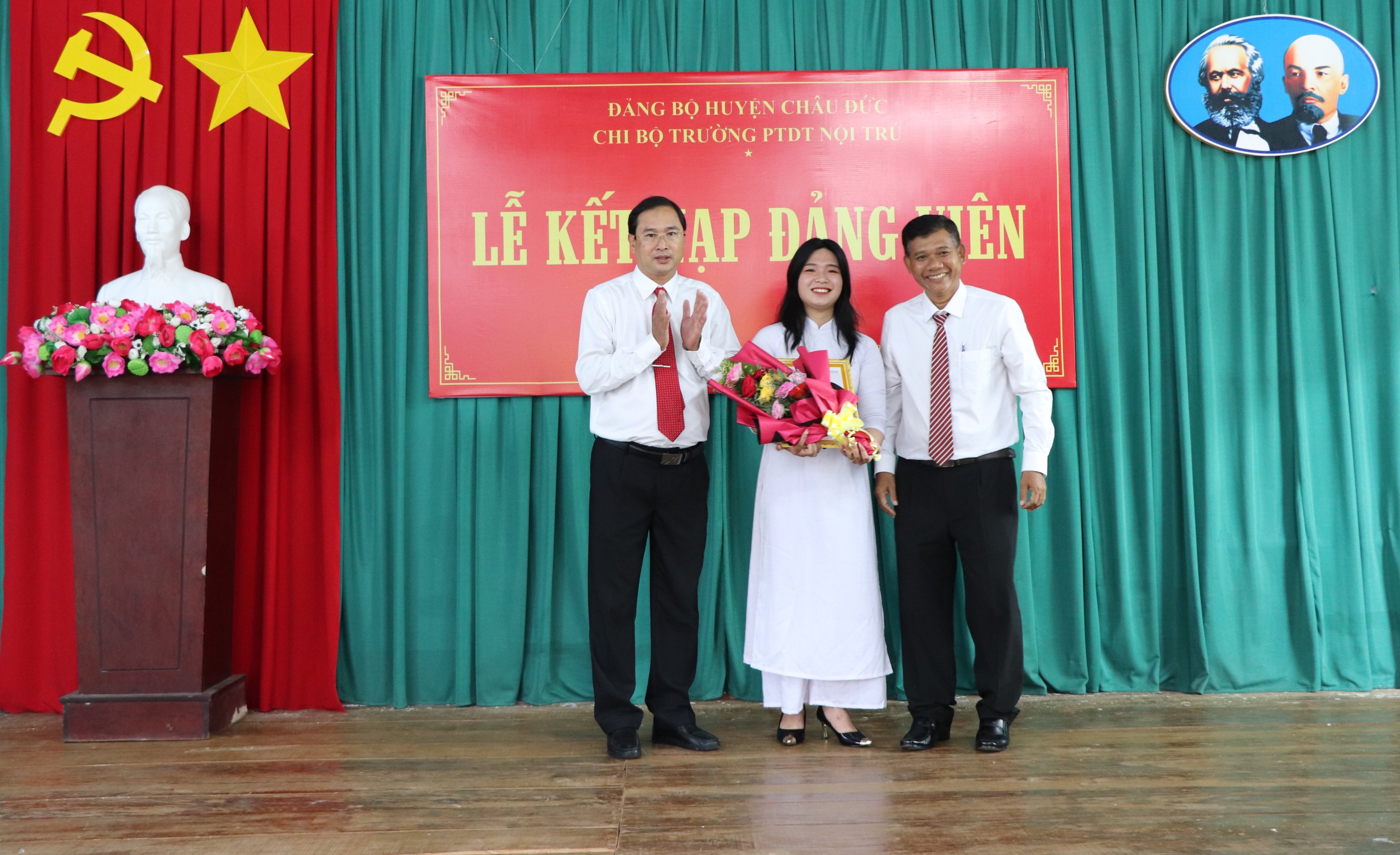 Ông Nguyễn Tấn Bản (bên trái), Phó Bí thư Thường trực Huyện ủy Châu Đức và ông Đào Văn Phước, Bí thư Chi bộ, Hiệu trưởng Trường PTDTNT tỉnh trao quyết định kết nạp Đảng và tặng hoa chúc mừng đảng viên Nguyễn Thị Hồng Hạnh.
