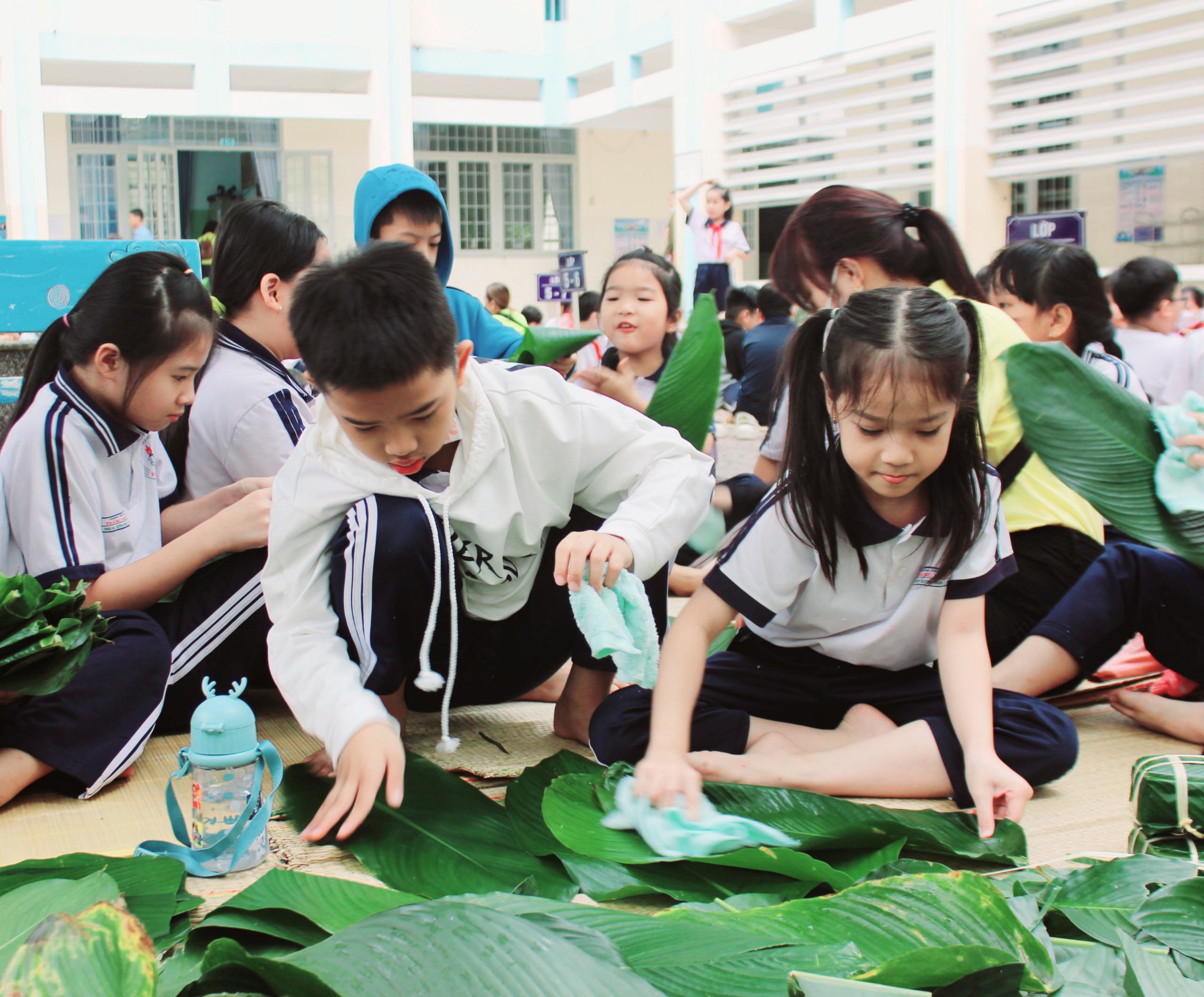 Các em học sinh tự tay lau từng chiếc lá dong để chuẩn bị gói bánh.