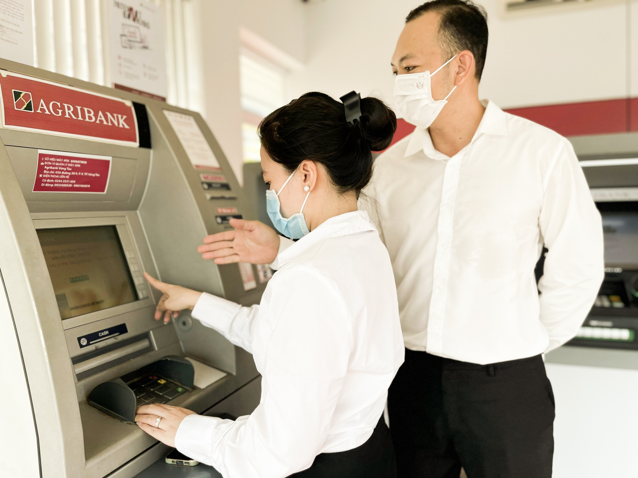 Nhân viên Agribank- chi nhánh Vũng Tàu (bìa phải) hướng dẫn khách hàng giao dịch trên máy ATM.