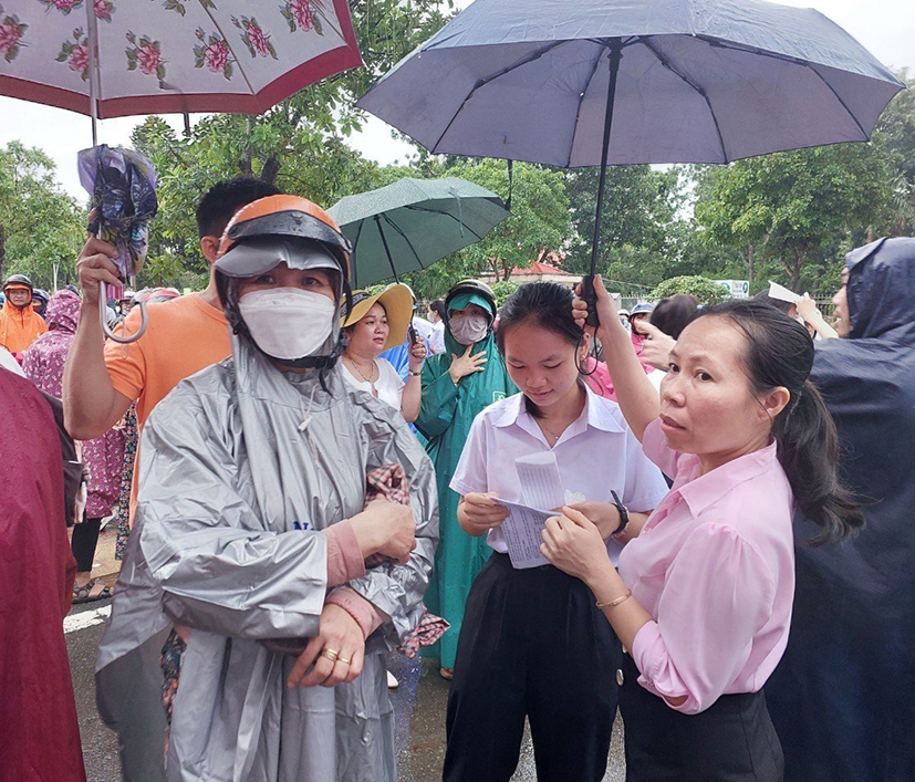 Phụ huynh tại điểm thi THPT Nguyễn Du đội mưa chờ thí sinh ra khỏi phòng thi.