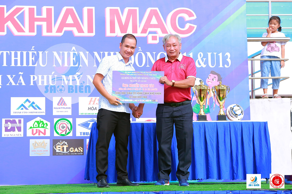 Đại diện Ban tổ chức tiếp nhận bảng tượng trưng học bổng cho các em HS vượt khó vươn lên tham dự giải bóng đá thiếu niên nhi đồng TX. Phú Mỹ