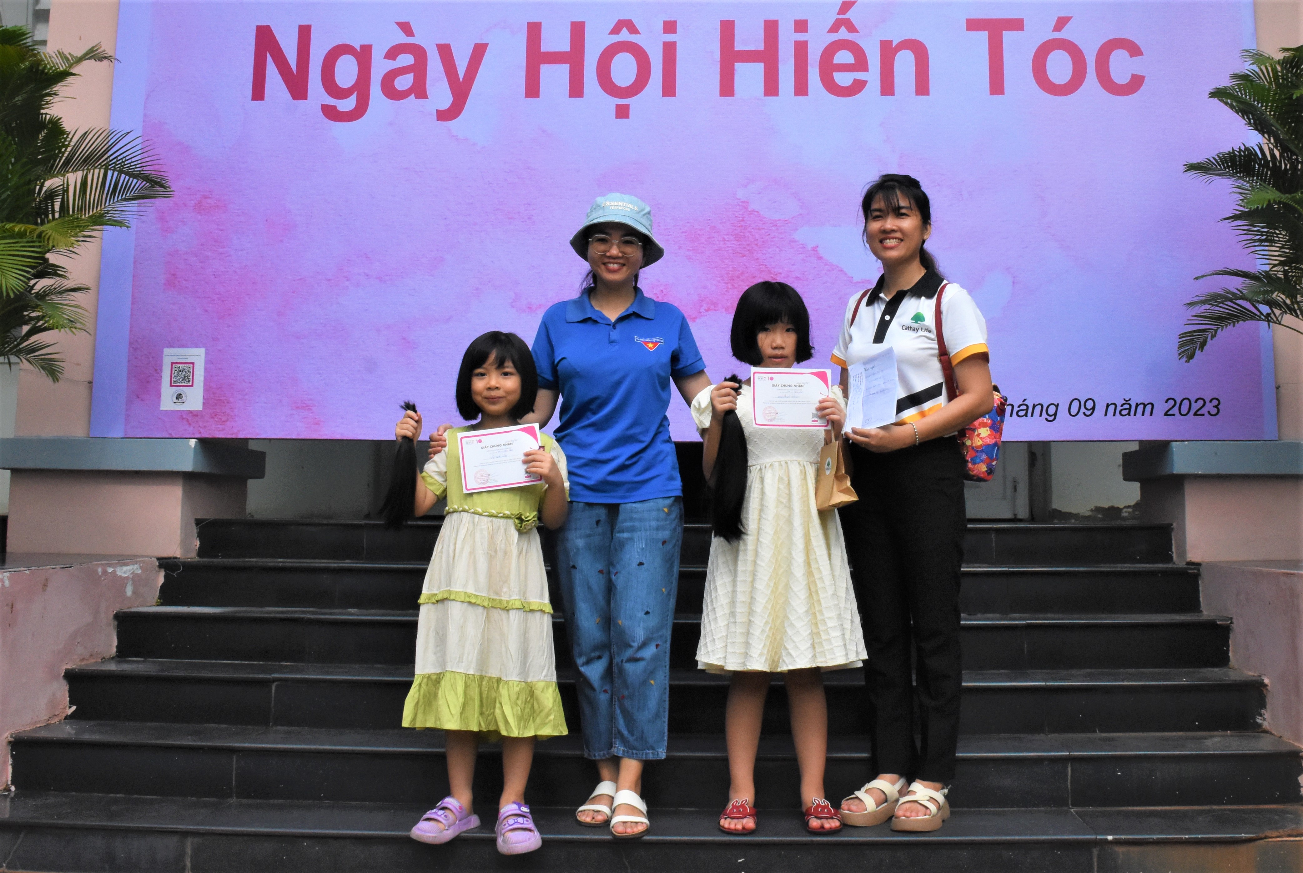 Tình nguyện viên nhí hào hứng khoe mái tóc hiến được bó cột cẩn thận và giấy chứng nhận hiến tóc tại ngày hội.