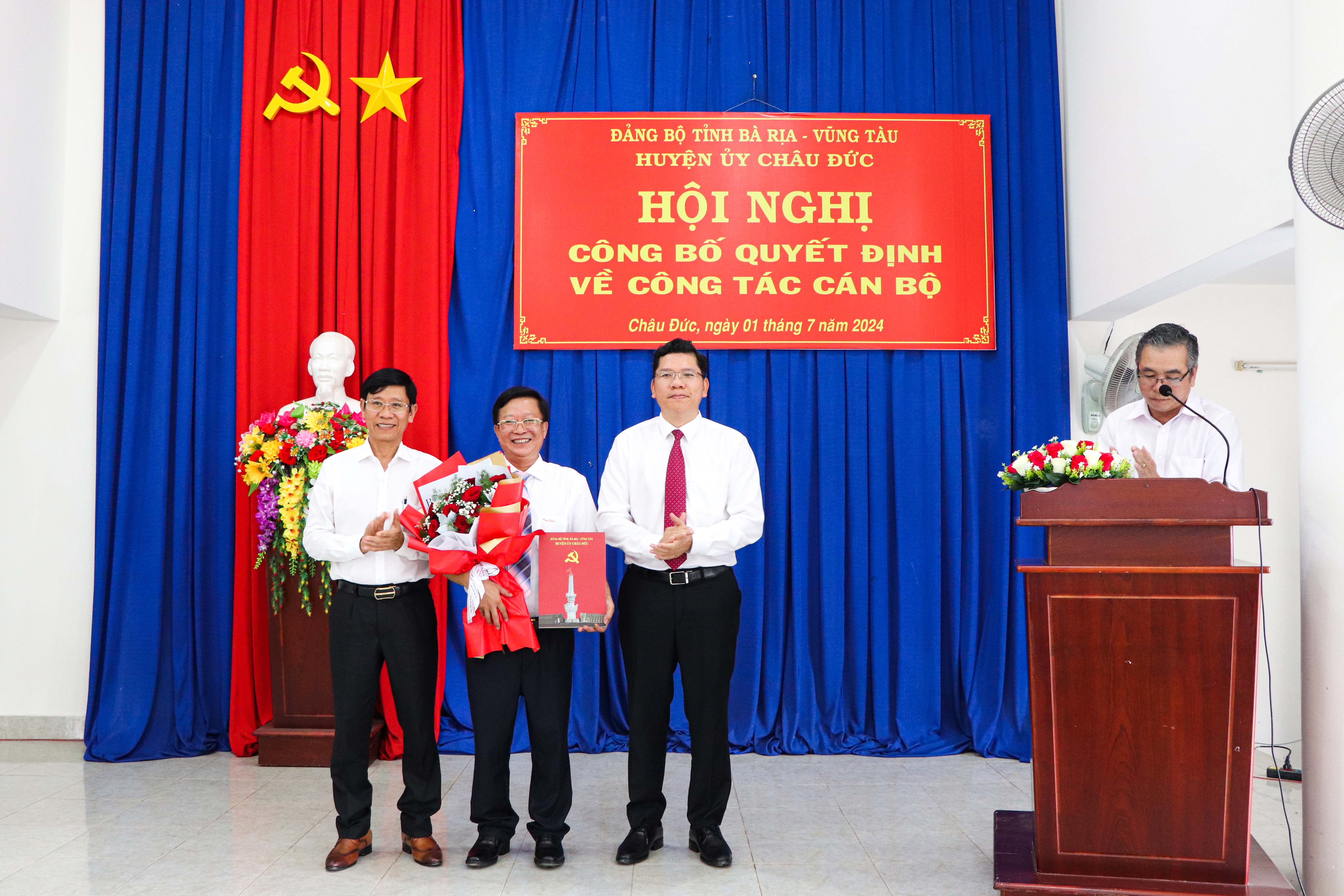 Ông Hoàng Nguyên Dinh (bên phải), Bí thư Huyện ủy, Chủ tịch HĐND huyện Châu Đức; ông Nguyễn Đức Tân, Phó Chủ tịch UBND huyện trao quyết định của Ban Thường vụ Huyện ủy Châu Đức và tặng hoa chúc mừng ông Ngô Văn Luận nhận nhiệm vụ mới.