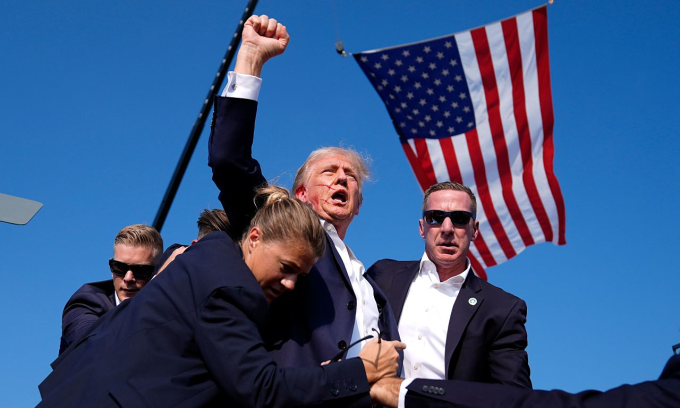 Ông Trump giơ nắm đấm khi được mật vụ dẫn khỏi sân khấu. Ảnh: AP