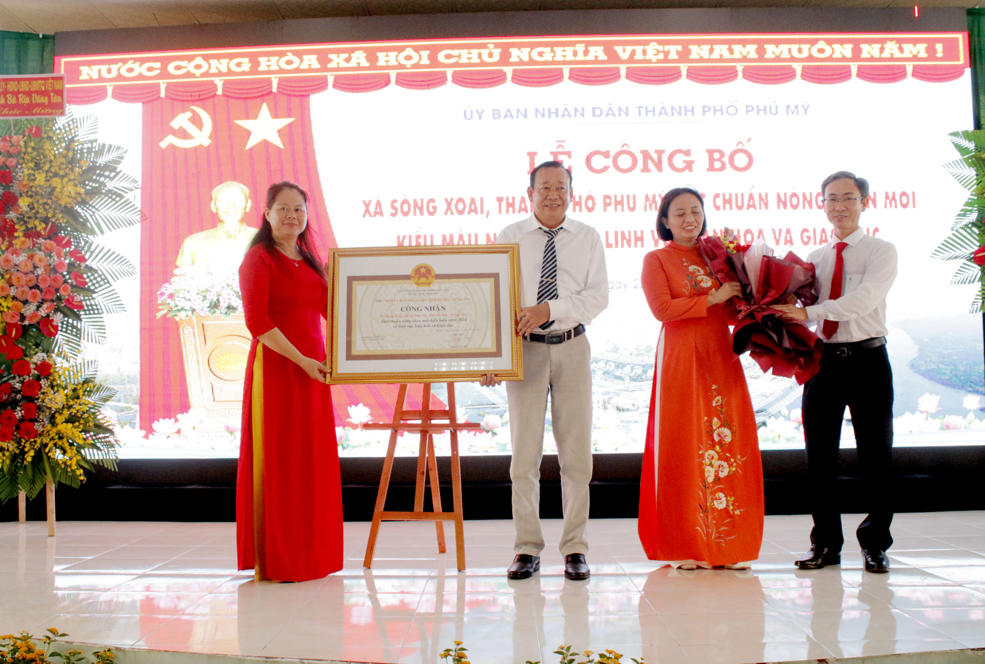 Đại diện tỉnh và TP. Phú Mỹ trao quyết định của UBND tỉnh công nhận xã Sông Xoài đạt chuẩn NTM kiểu mẫu năm 2024 và hoa chúc mừng cho Đảng bộ, chính quyền và Nhân dân xã Sông Xoài.